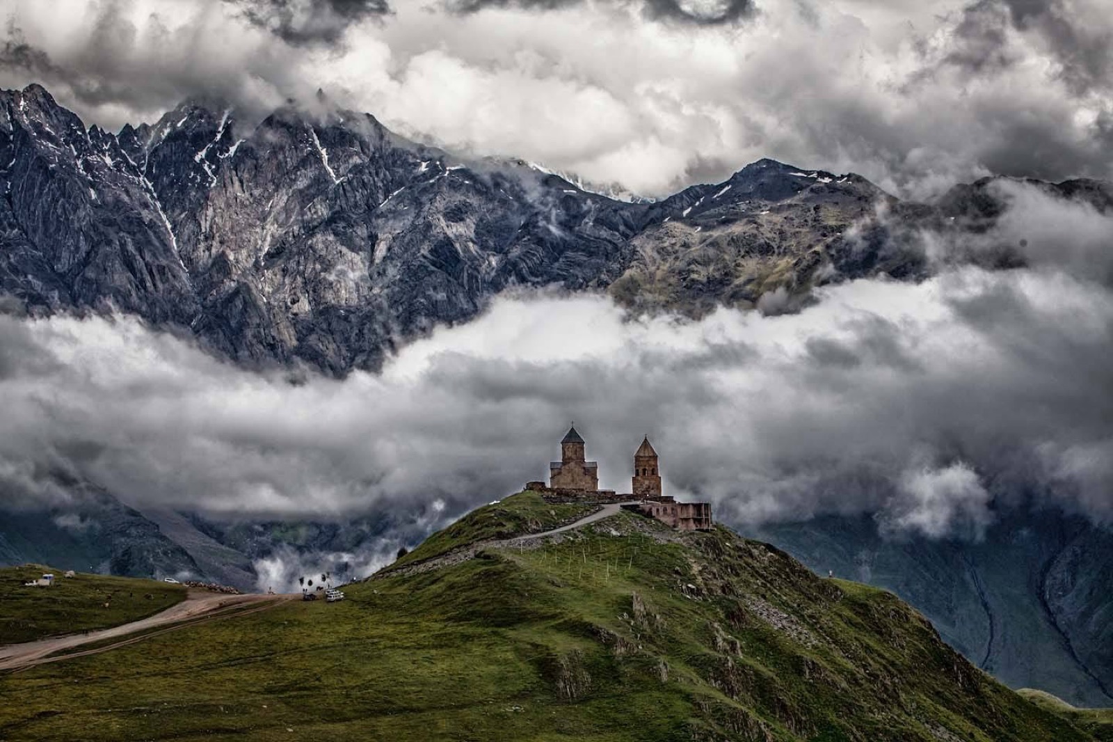 Gergeti Trinity Church on its green hill below the cloud-wrapped Caucasus near Kazbegi, Georgia