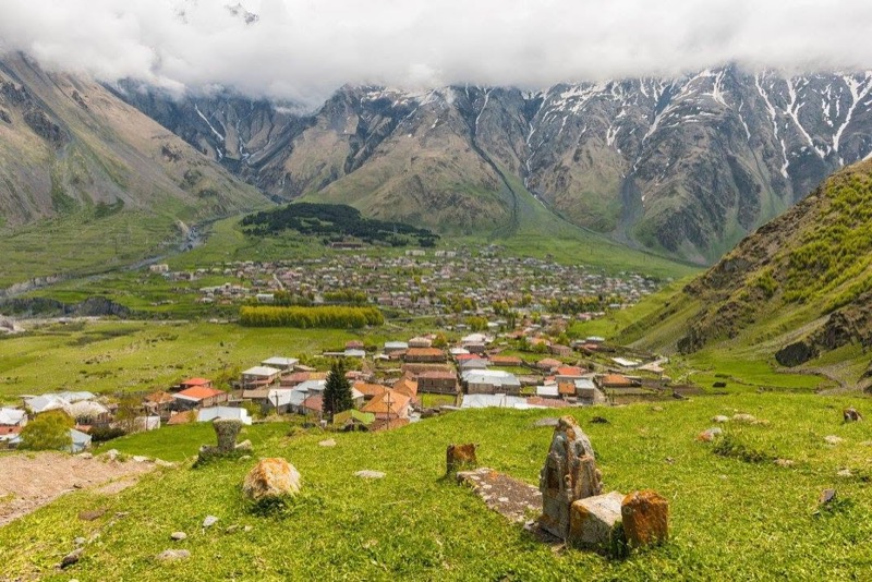 A village in a green valley ringed by the snow-capped peaks of the Greater Caucasus