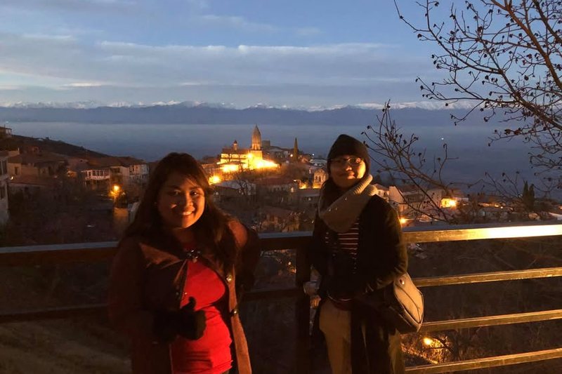 A couple at a viewpoint over the lit town of Sighnaghi and the Caucasus at dusk